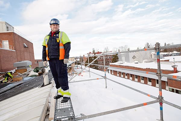 Fyra våningar upp pågår reparationer av taket. Snö och is ökar halkrisken. Räcket består av väl förankrade rör och håller även om huvudskyddsombudet Lasse Johansson ramlar mot det.   Foto: TOMAS BERGMAN